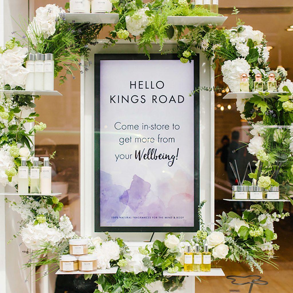 An Ultra High Brightness Digital Advertising Screen in a shop window surrounded by flowers.