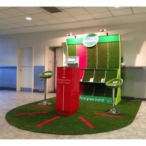 A custom exhibition display and red plinth on top of artificial grass.