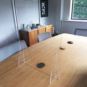 A clear acrylic desk sneeze guard sat on a table in an office.
