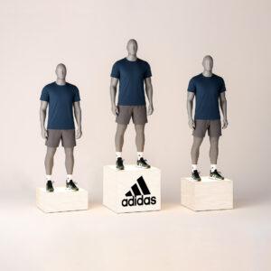 Set of three branded adidas logo illuminated plywood display plinths with mannequins wearing navy shirts and gray shorts, showcasing modern retail presentation stands with soft lighting.
