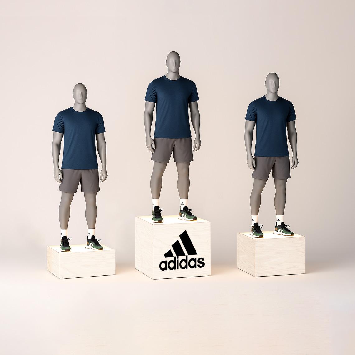 Set of three branded adidas logo illuminated plywood display plinths with mannequins wearing navy shirts and gray shorts, showcasing modern retail presentation stands with soft lighting.