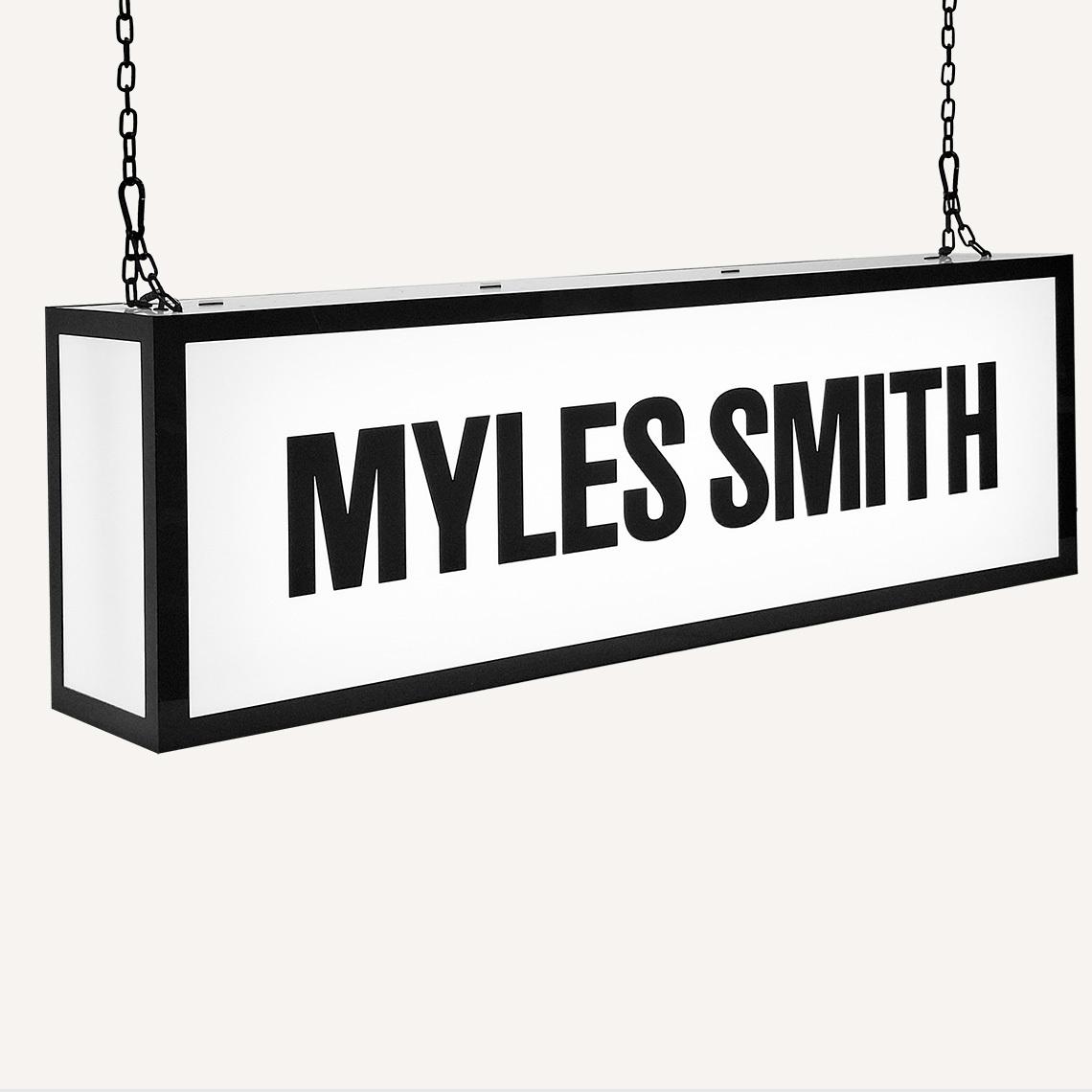 A ceiling hanging illuminated sign with "Myles Smith" on the front.