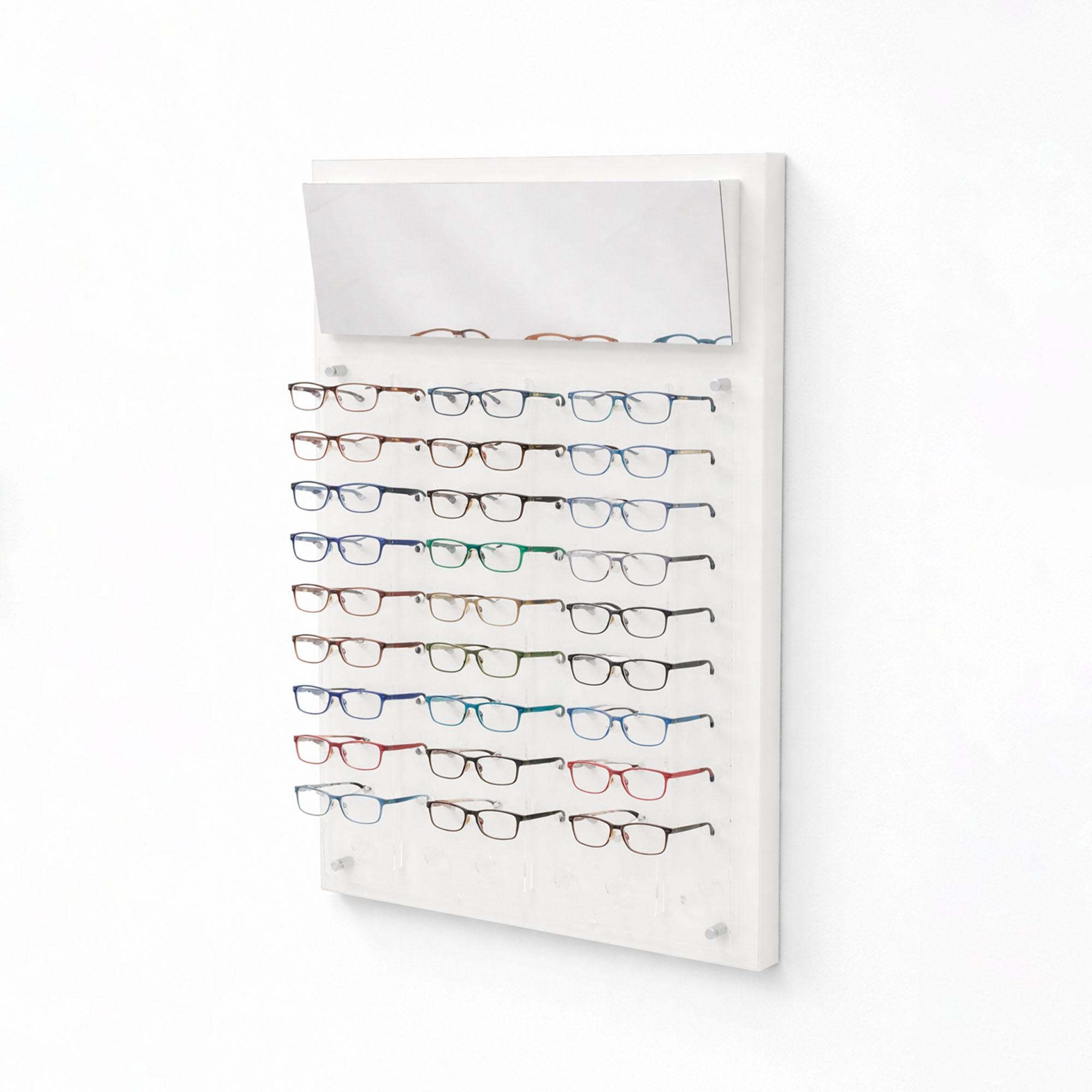 Angled view of wall-mounted white glasses display board with mirror, showcasing multiple rows of eyeglass frames on transparent holders