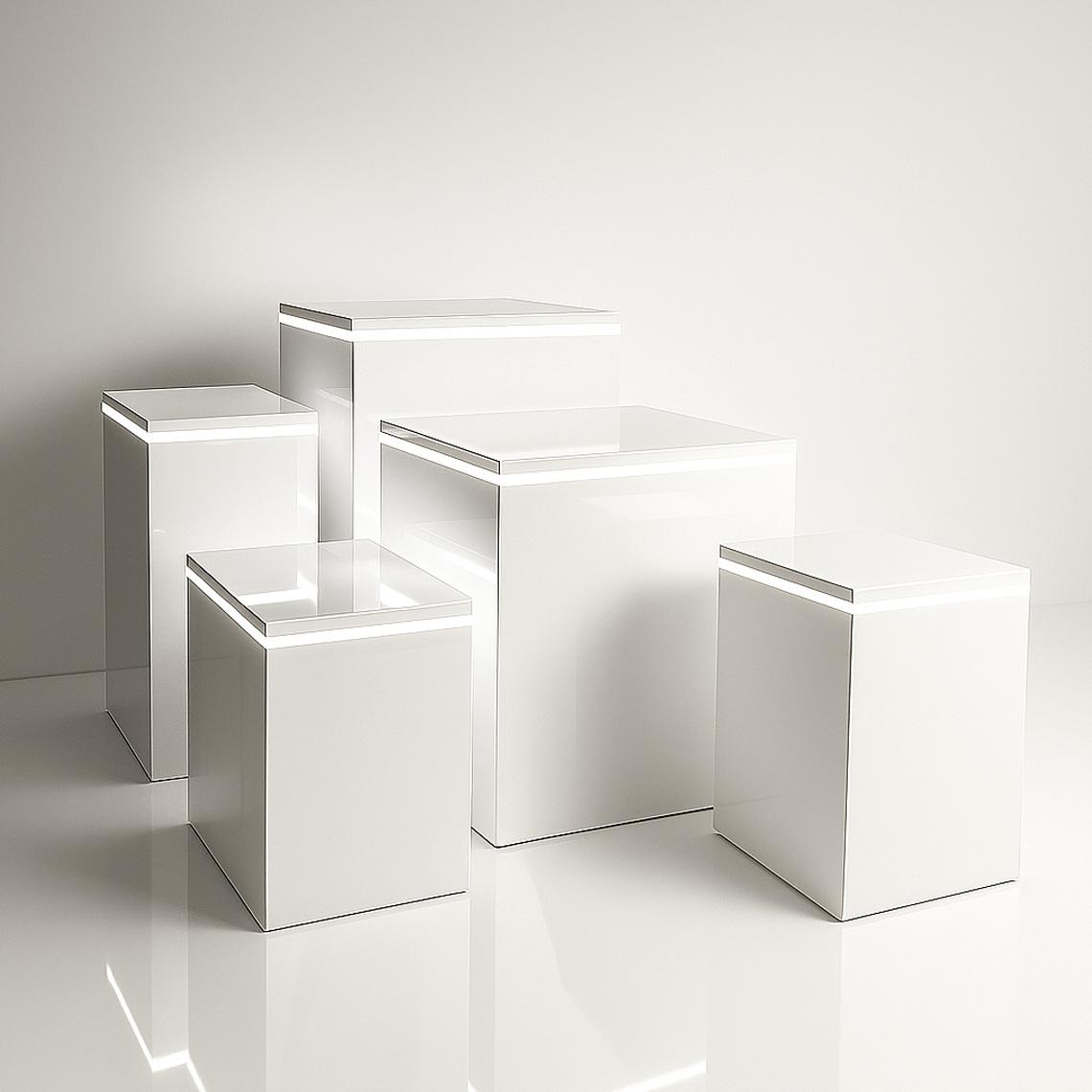 Set of white high gloss display plinths with built-in LED light strips near the top edges, arranged in varying heights in a clean studio setting.