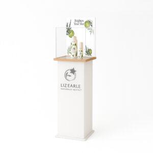 Liz Earle Naturally Active skincare display stand featuring wooden top & mirror display top, clear acrylic case, and botanical ‘Brighten Your Skin’ printed backdrop shown in an interchangeable graphics trap and branded header on a frosted white plinth.