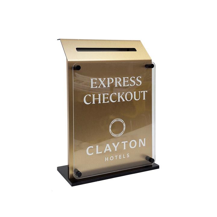 A gold express checkout hotel key drop box with a black base and a "clayton" logo on it.
