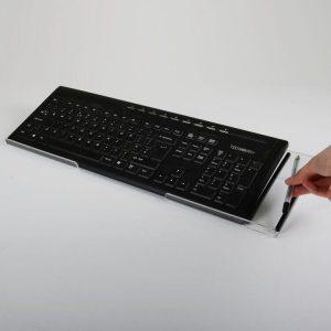 A clear keyboard rest holding a black keyboard with a hand putting a pen into the ribbed pen holder.