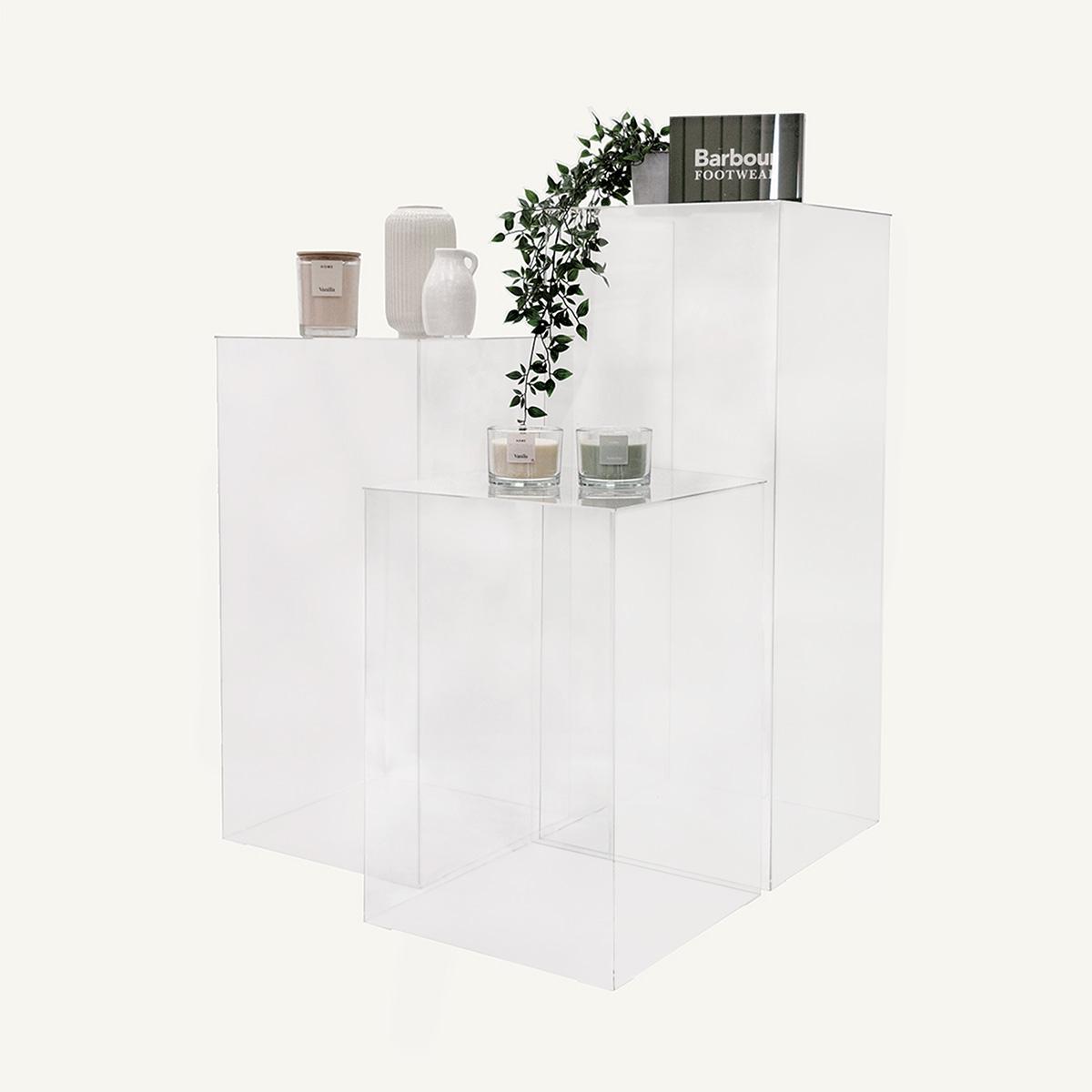Three Acrylic Display Plinths with Barbour branding block, candles, vases and a plant on display.