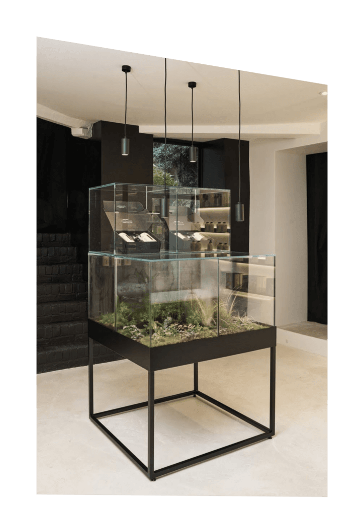Contemporary glass display unit with black metal legs displaying beauty products in a salon.