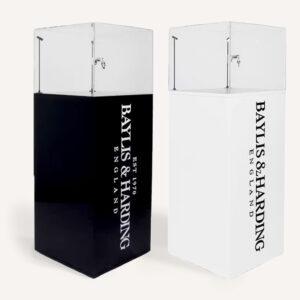 Two lockable display case plinths, one black and one white, each with a clear acrylic showcase and Baylis & Harding branding on the pedestal.