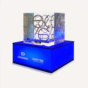 A blue illuminated pedestal base with a transparent decorative block with copper rings on top with an "Ametek logo".