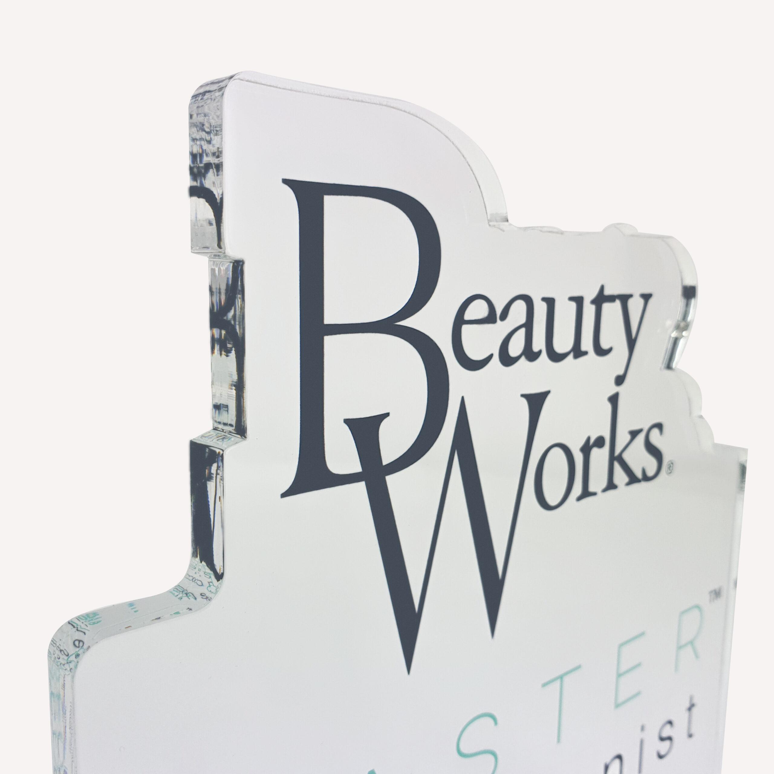 A close up of a solid clear acrylic, custom made award with "beauty works" logo on the front.