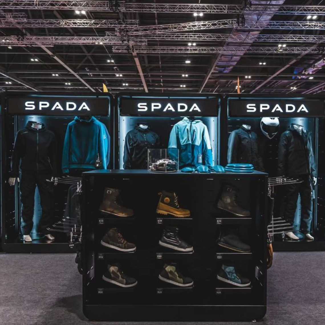 A front facing picture of a Feridax Spada exhibition display, showcasing clothing and shoes under lighting.
