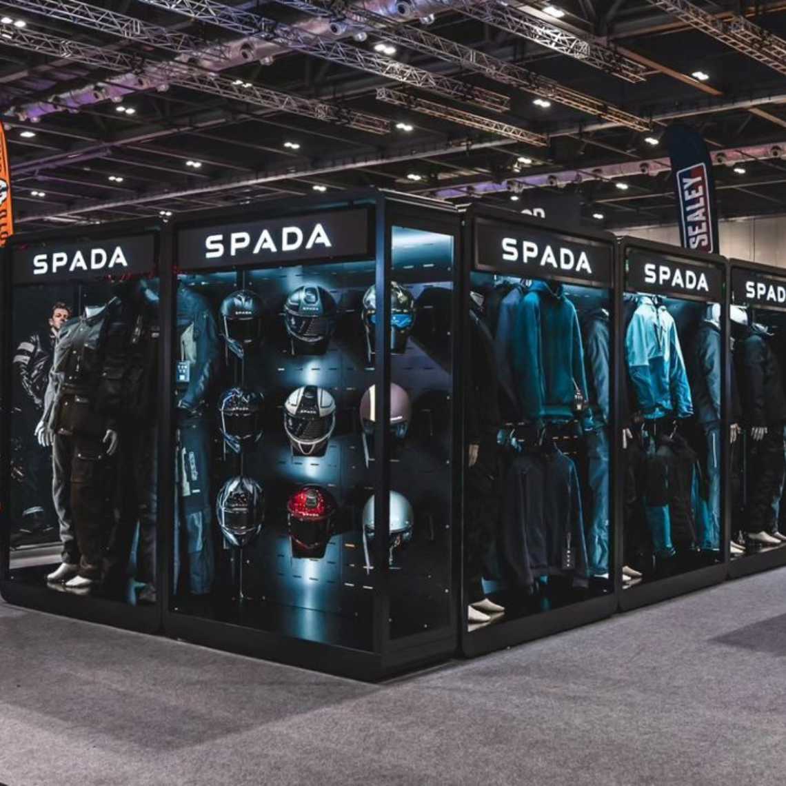 An angled wide view of a Feridax Spada exhibition retail display, showcasing clothing and bikers helmets under lighting.