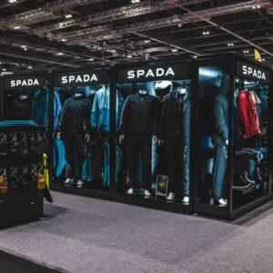 A wide corner angle of a Feridax Spada exhibition retail display, showcasing mannequins, clothing, motorbike helmets and shoes under lighting.