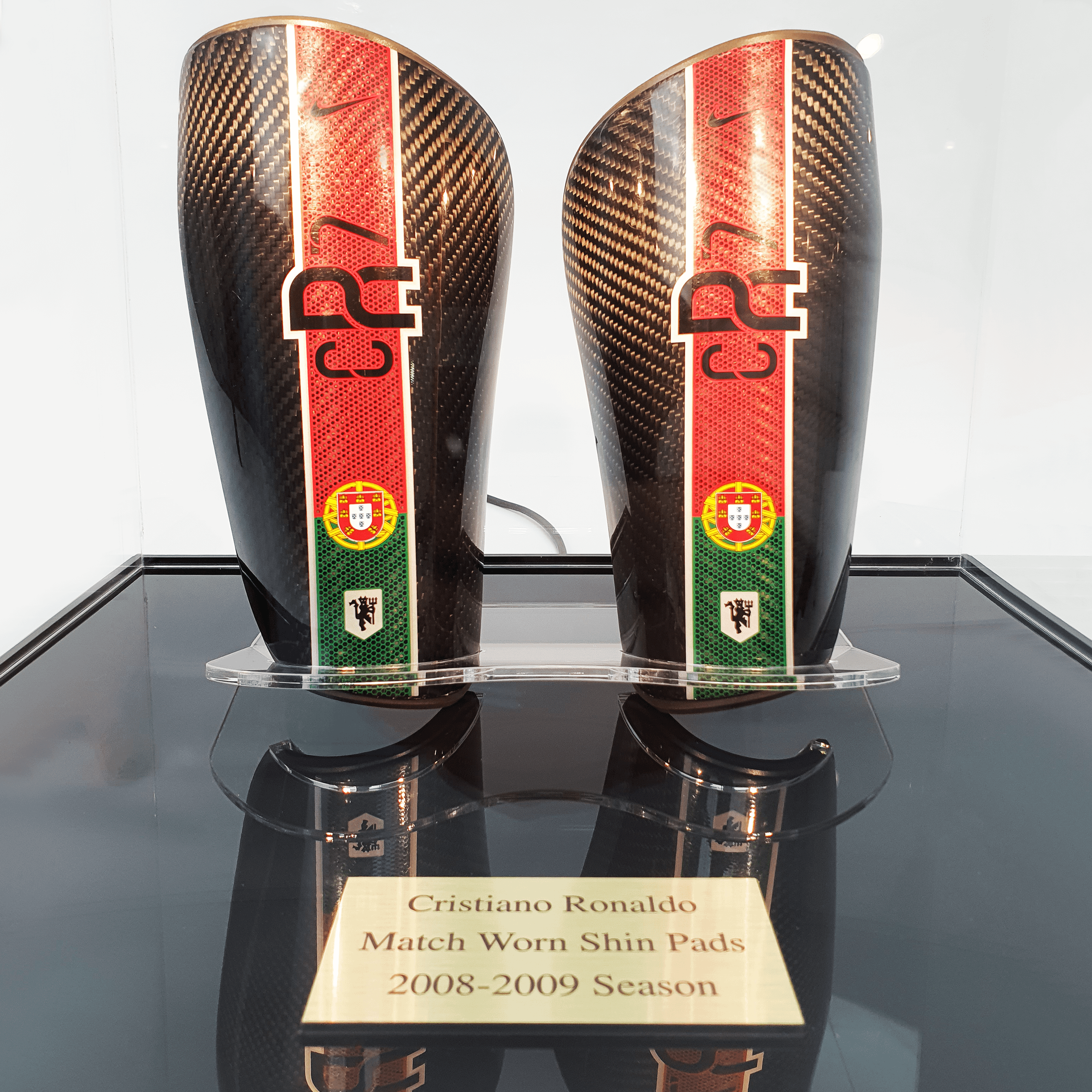 A close up, front facing view of Cristiano Ronaldo’s match-worn shin pads in a collector's acrylic display case with a black base and personalised plaque.