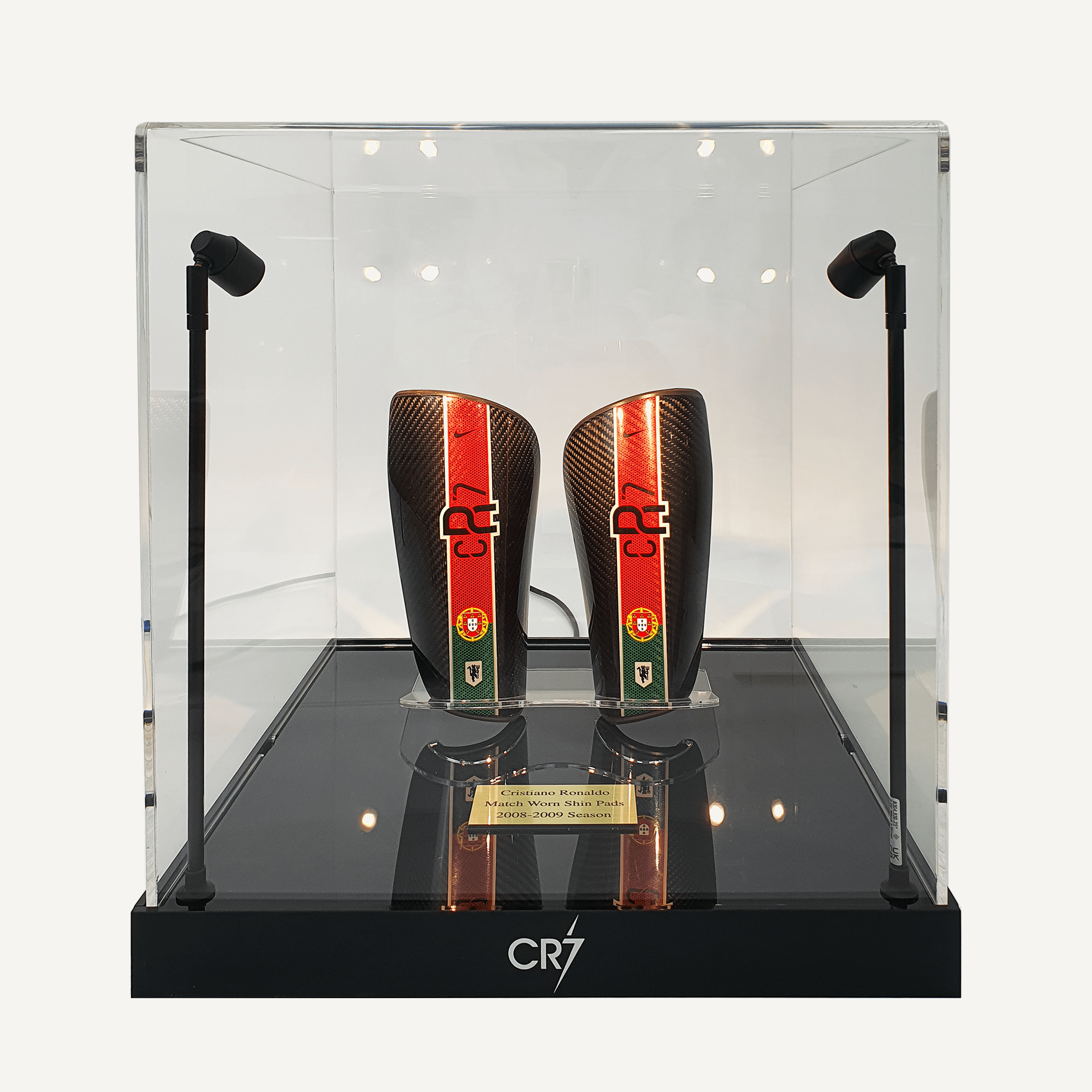 A front facing view of a collectors acrylic display case with spotlights, a black customisable base and personalised plaque, featuring Cristiano Ronaldo’s match-worn shin pads.