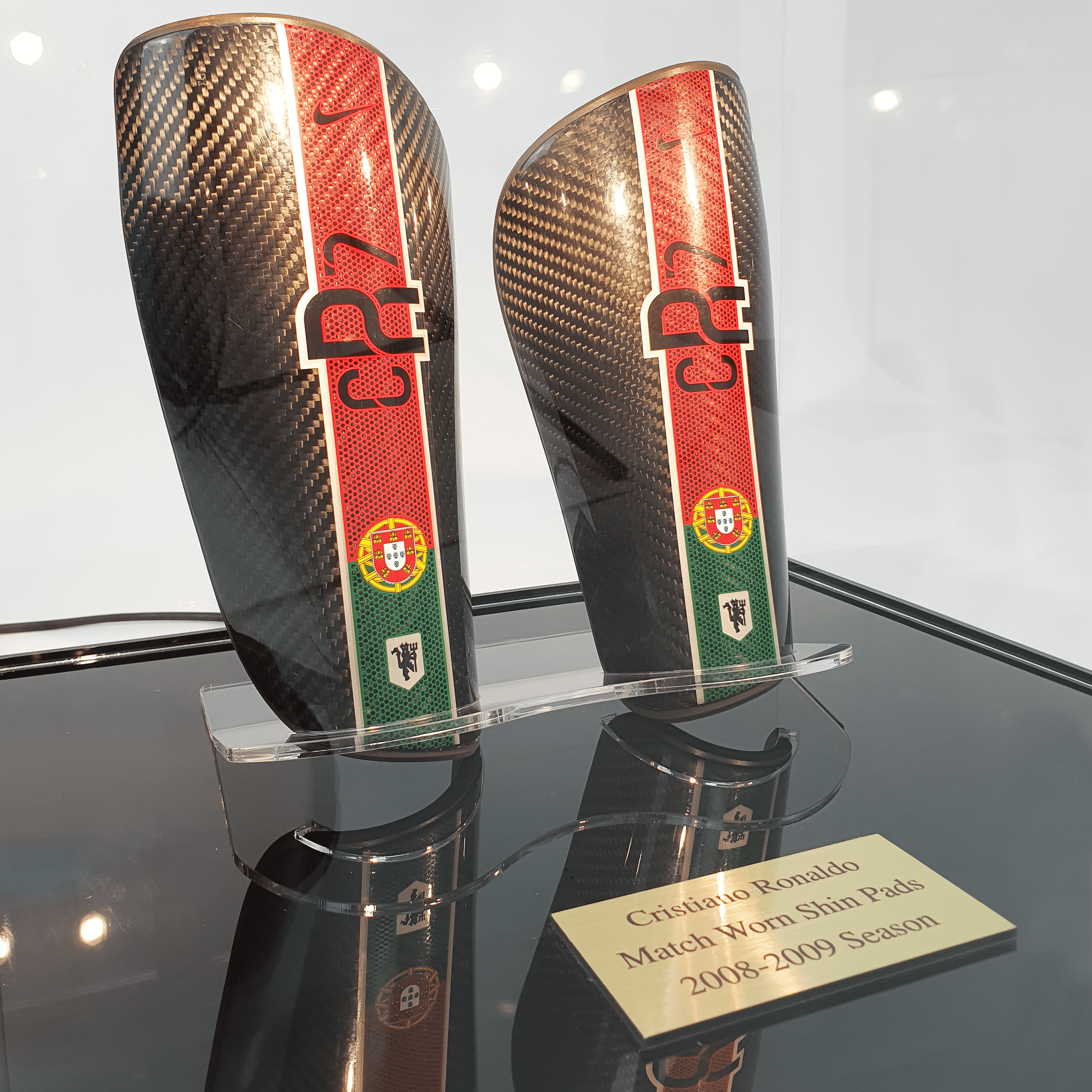 A close up of Cristiano Ronaldo’s match-worn shin pads in a collectors acrylic display case with a black base and personalised plaque.