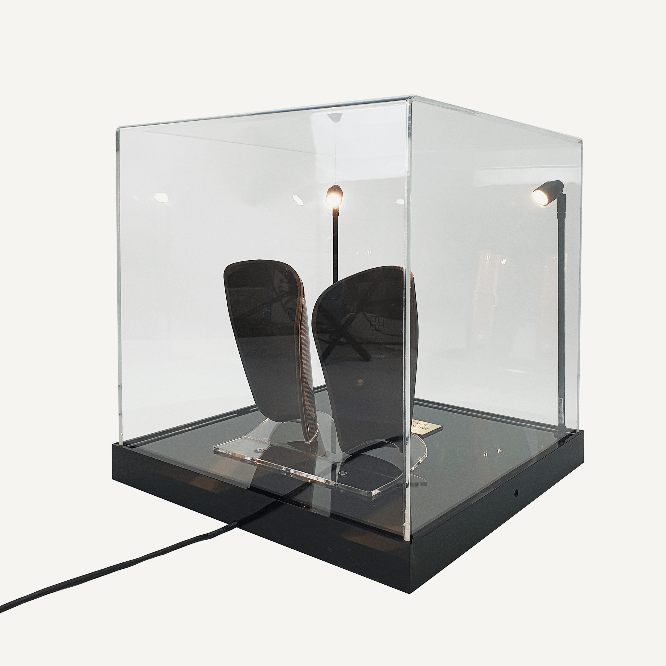 A back view of a collectors acrylic display case with a wire coming out of the back, spotlights, a black customisable base and personalised plaque, featuring Cristiano Ronaldo’s match-worn shin pads.