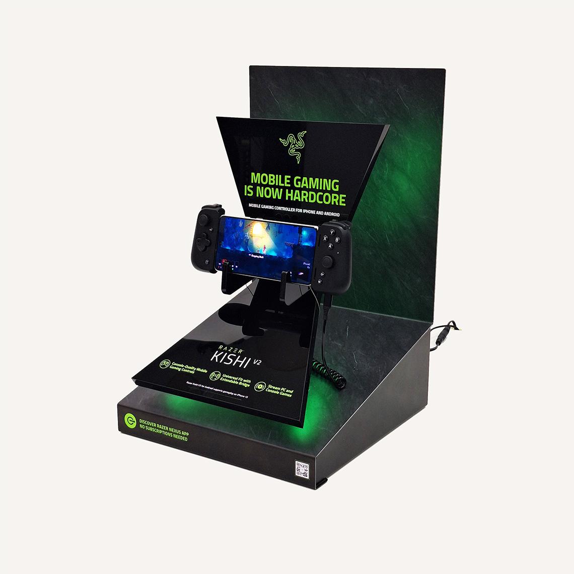 Left facing view of a gaming console display stand featuring the Razer Kishi V2 mobile gaming controller with a mounted smartphone showing gameplay.