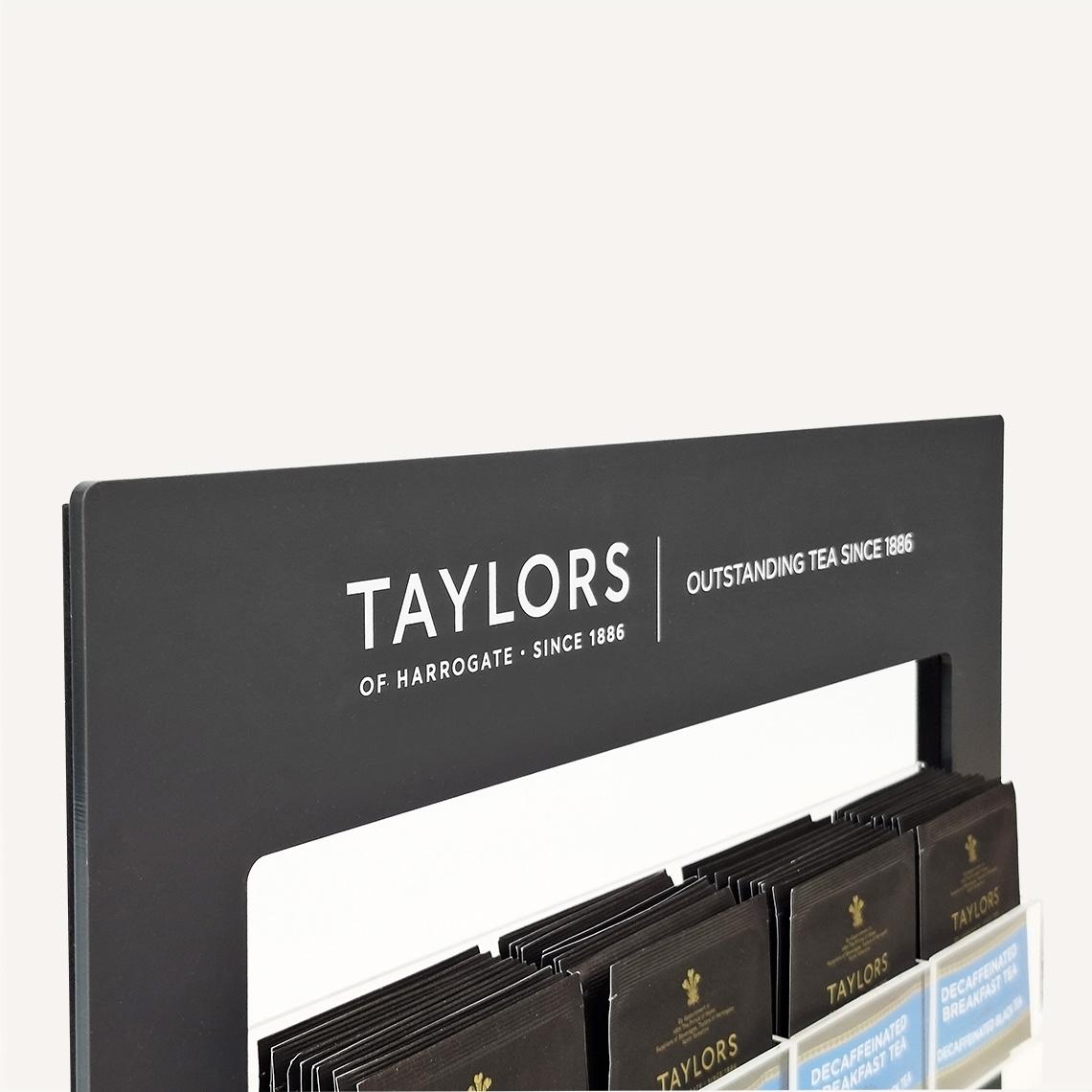 A close up view of the top of a black Taylors of Harrogate tea bag pos display stand with custom branding and clear acrylic tea bag holders.