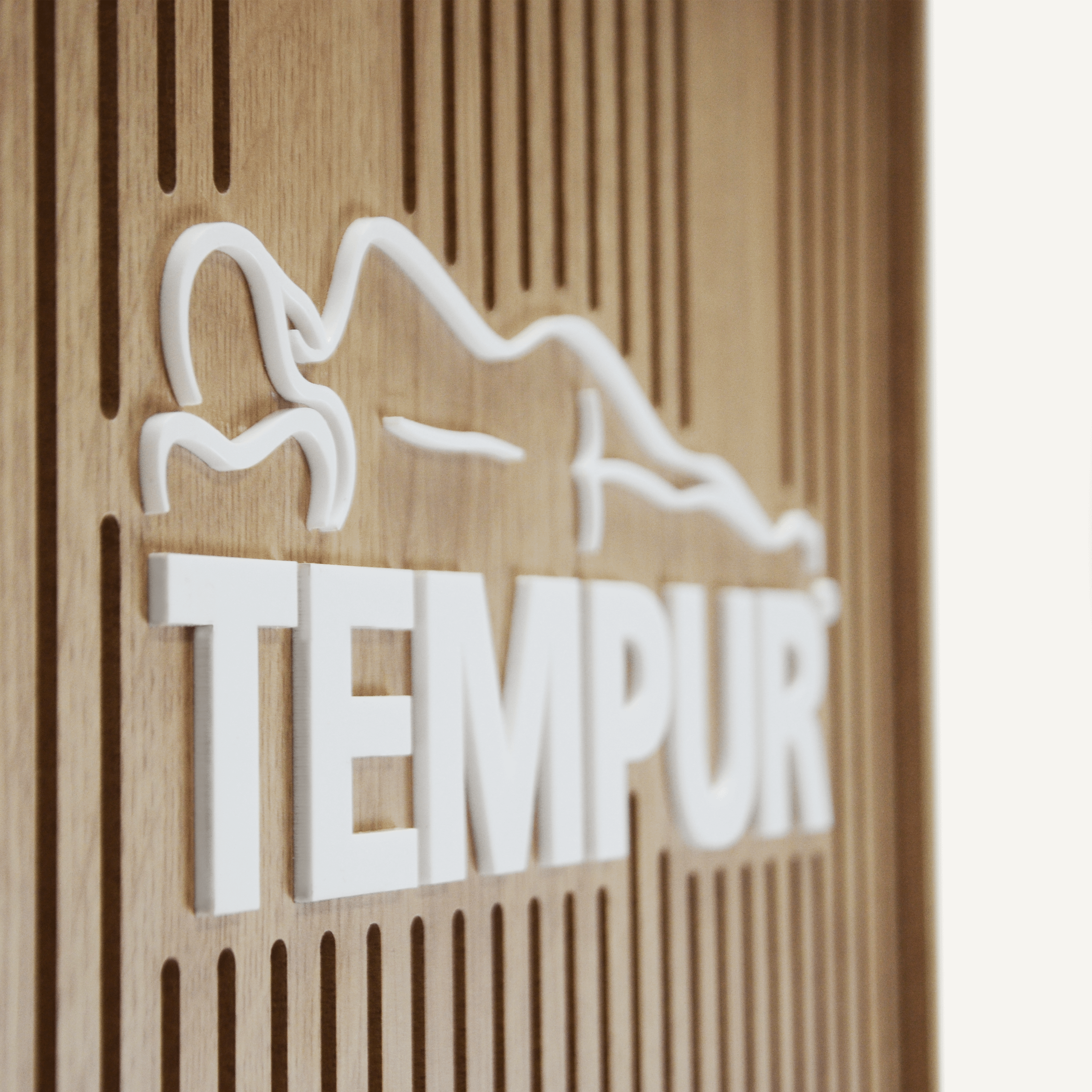 A close up of a 3D acrylic logo saying "Tempur" on a plywood slatted rotating POS display.