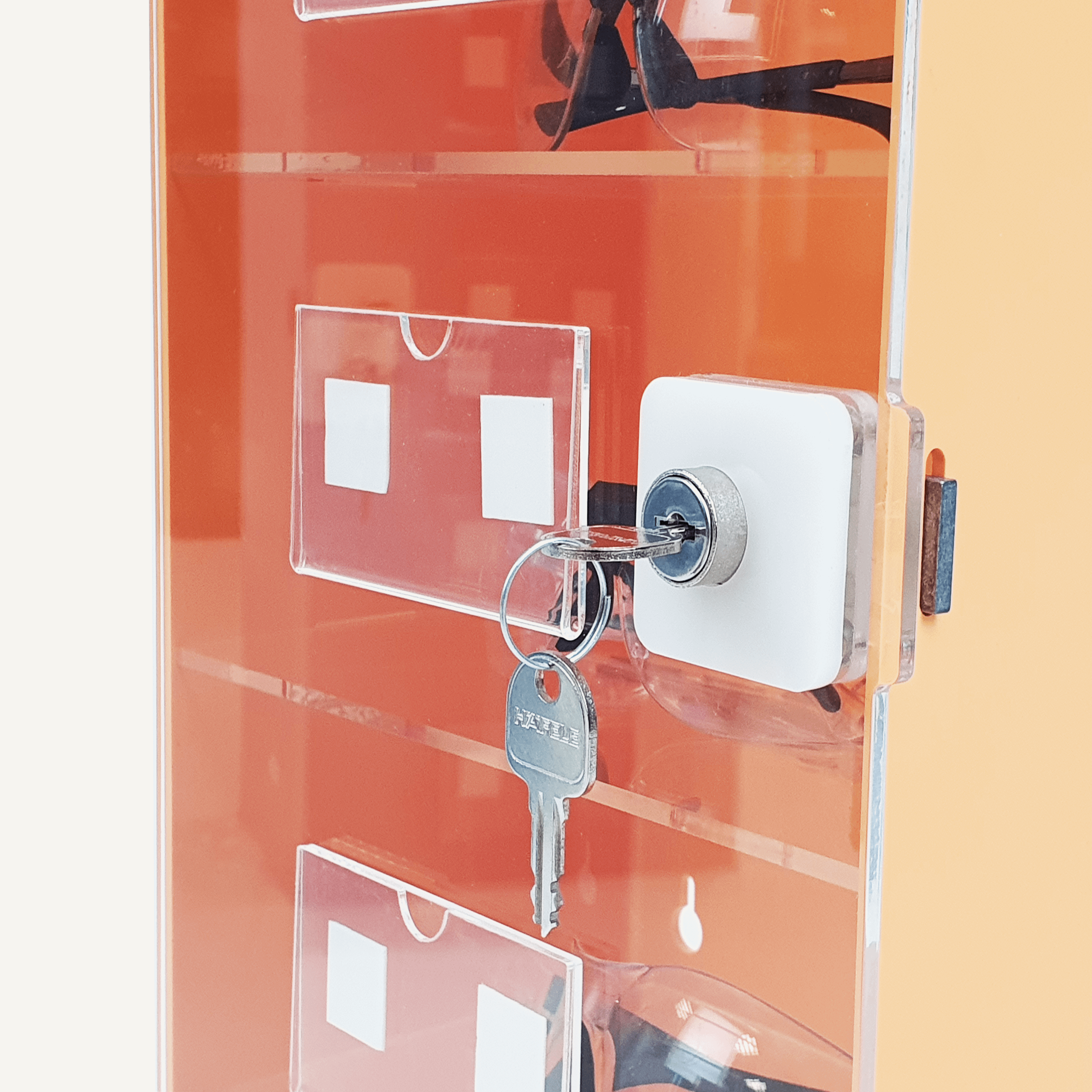 A close up of a lock and key on an orange and clear acrylic PPE storage cabinet with safety goggles inside.