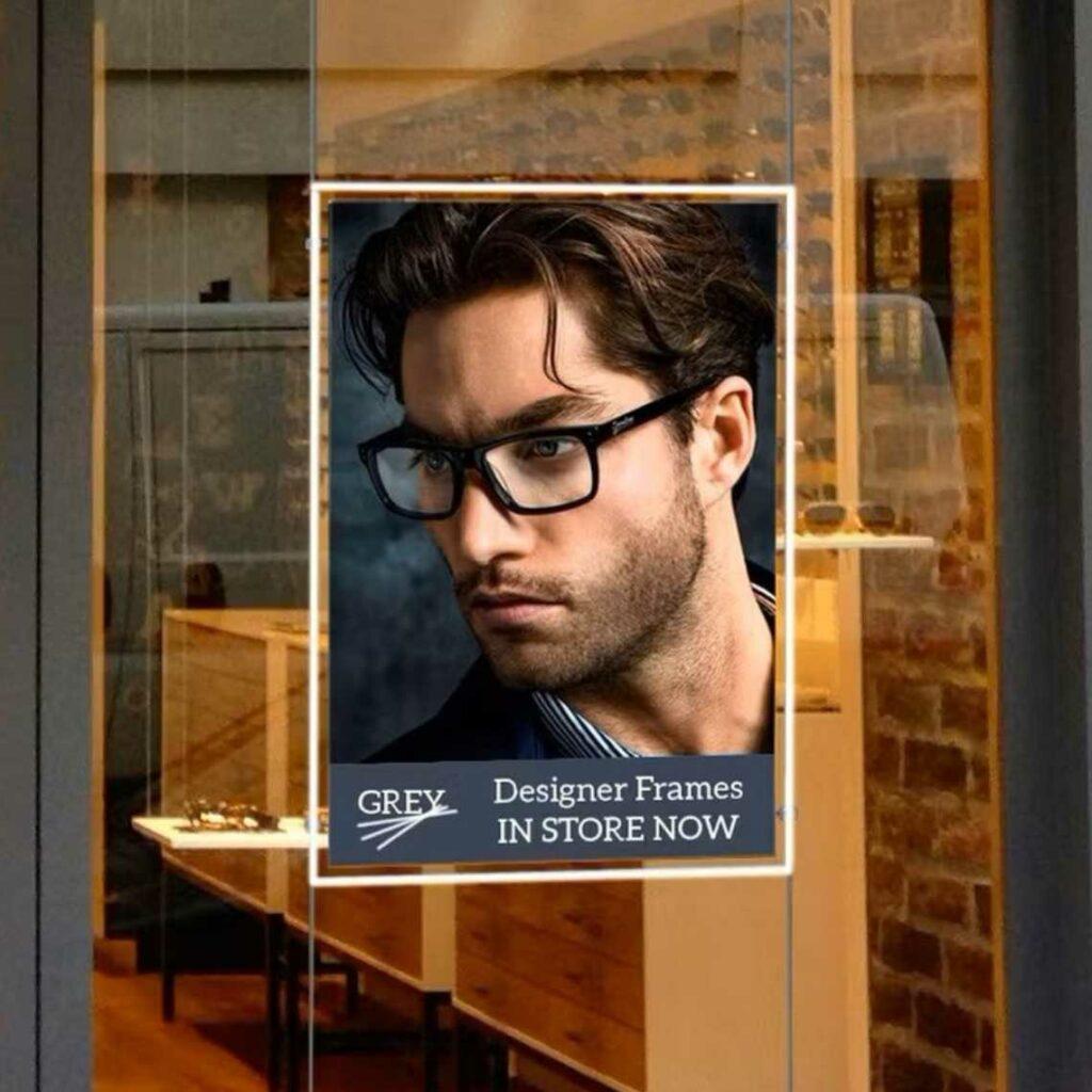 A LED window pocket frame advertising some glasses on a man in front of an opticians.