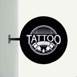 An outdoor illuminated lightbox sign with "tattoo" written on.
