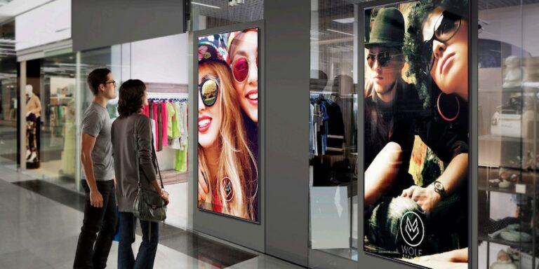 People looking at digital advertising screens outside of a shop.