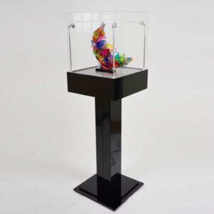 A black plinth pedestal with a protective cover and a decorative ornament on display.