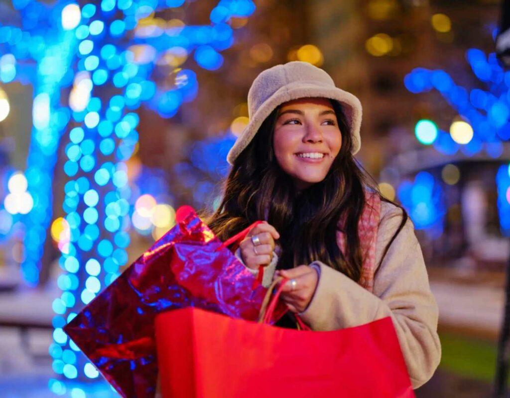 A smiling girl holding shopping bags and dressed in winter clothing.
