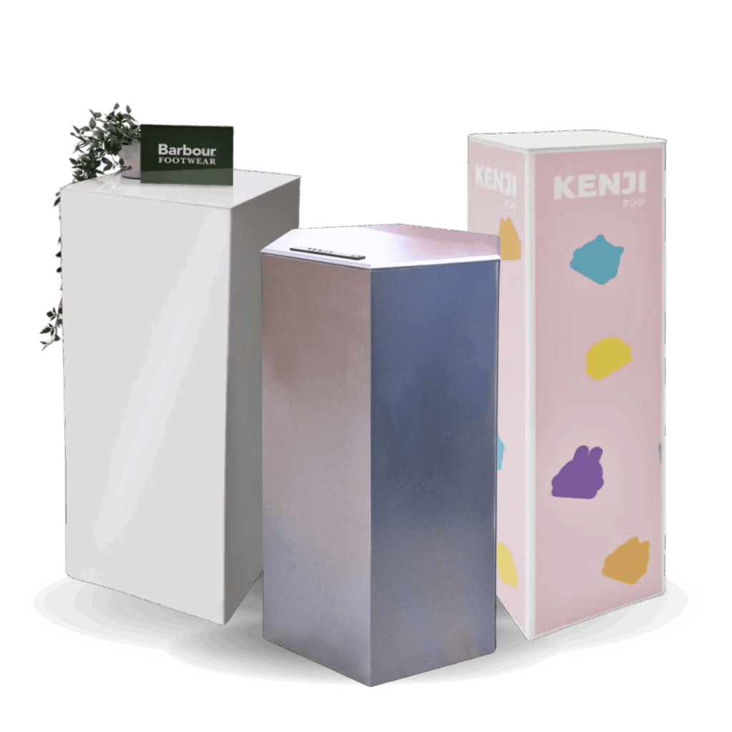 Three display plinth pedestals. One pink branded plinth, one white acrylic plinth & one custom branded metallic hexagonal plinth.