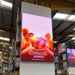 Portrait LED advertising screen mounted on a warehouse pillar displaying a Cîroc campaign—high-brightness retail signage.