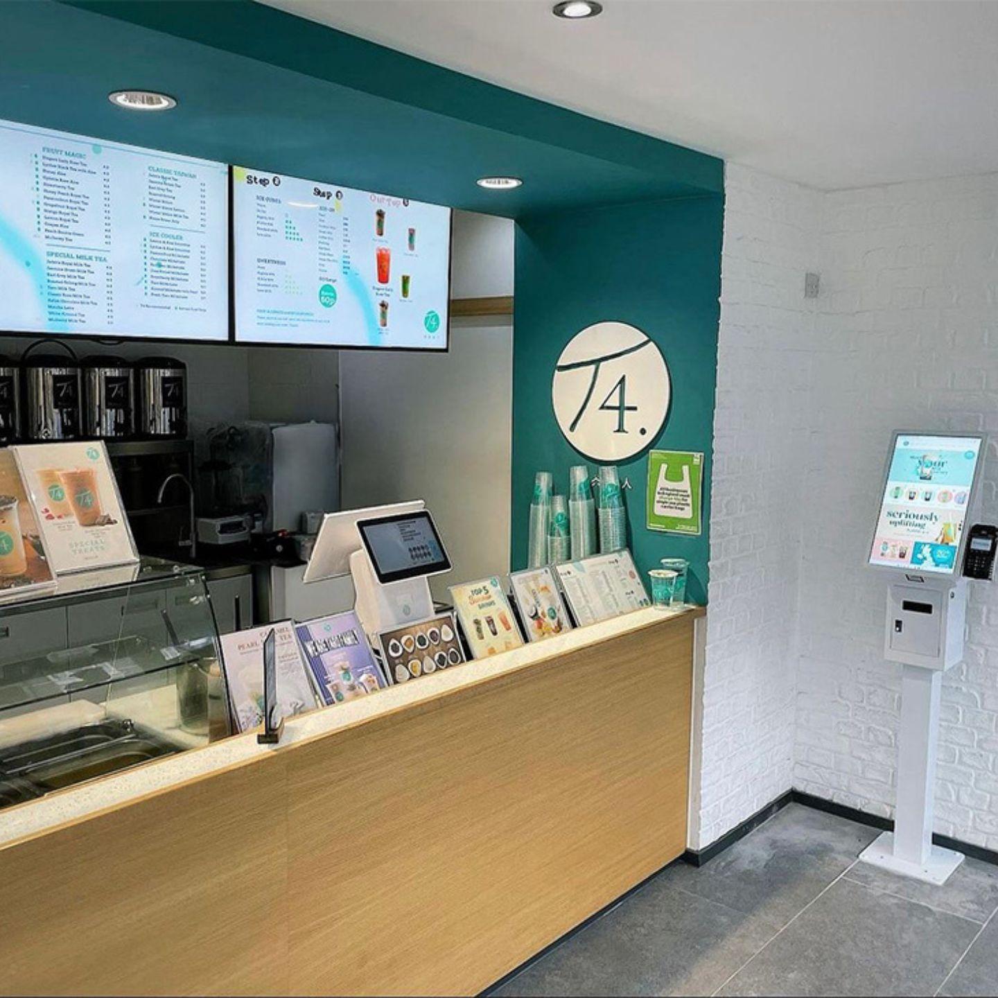 Compact touch screen checkout kiosk in café—self-service ordering terminal beside counter and digital menu boards, card payment enabled.