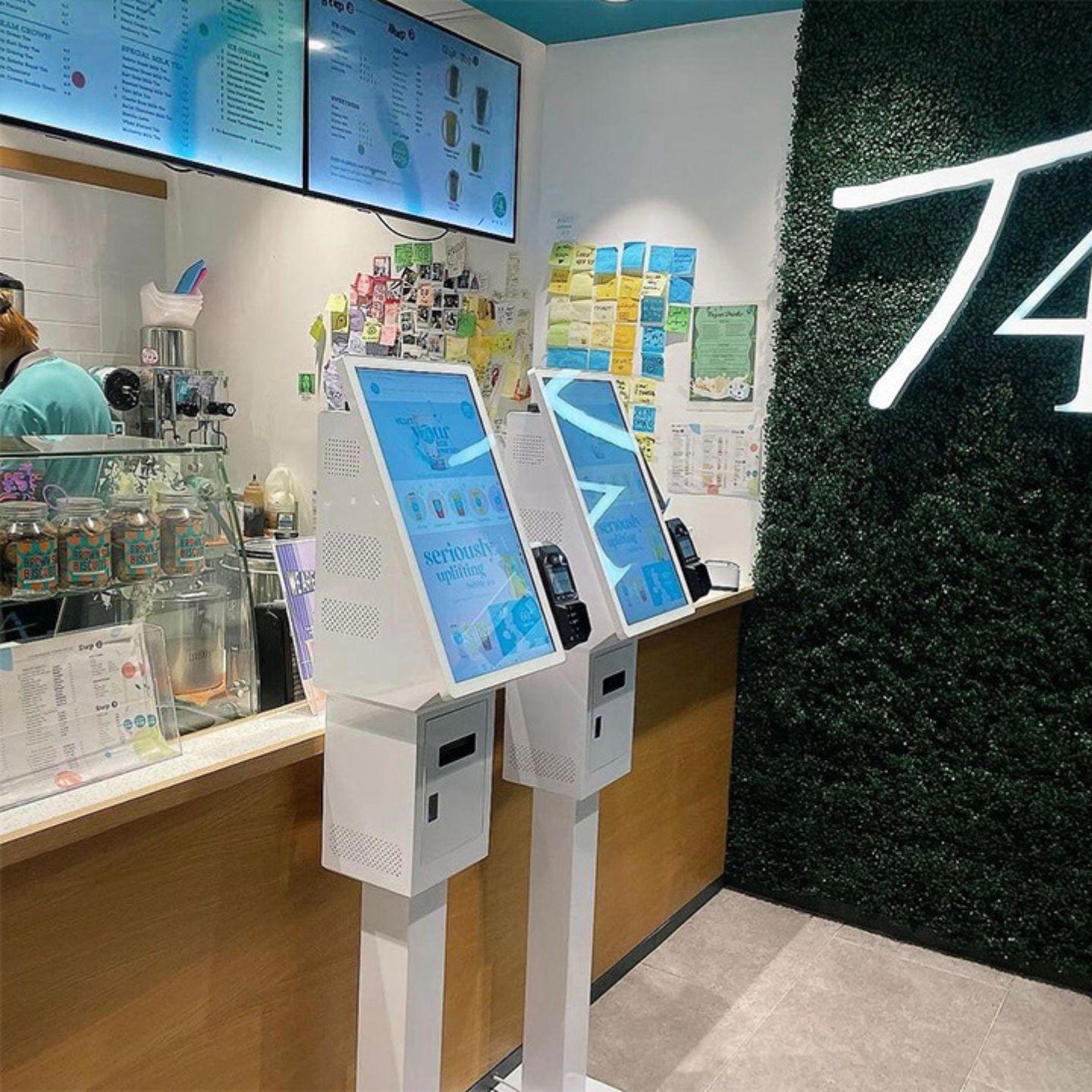 Touch screen checkout kiosks in bubble tea shop—two freestanding self-service ordering stations with payment terminals at the counter.