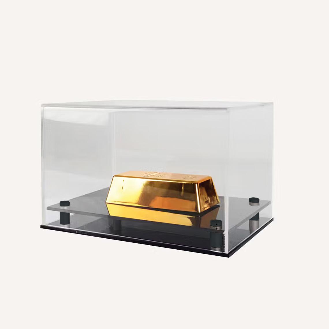 Transparent rectangular acrylic display case featuring a metallic gold model on a raised black base, set against a light background.