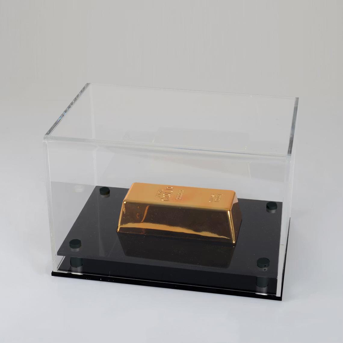 Transparent acrylic display case featuring a polished golden model on a glossy black base, photographed from an elevated angle against a neutral background.