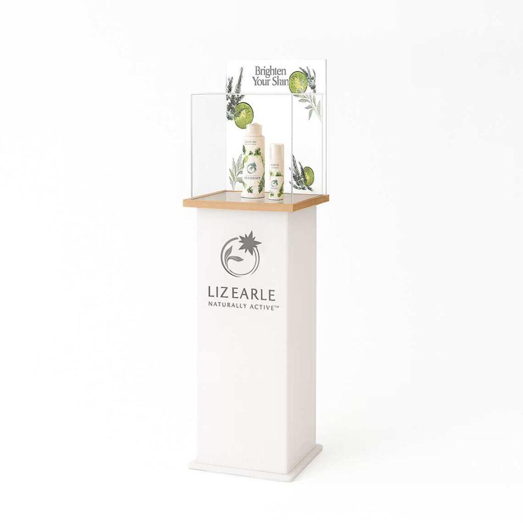 A custom Liz Earle branded frosted white product display plinth with a clear display case on top, featuring skincare products on display and an interchangeable graphics trap.