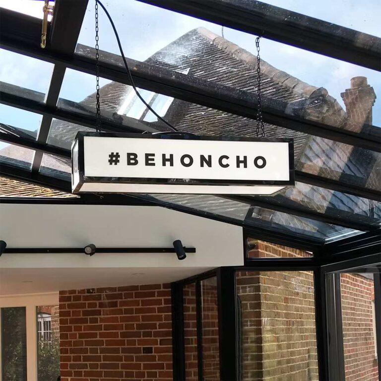 A ceiling hanging illuminated lightbox with #behonco custom branding.