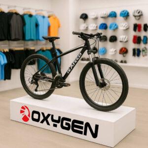A bike on a white MDF podium in a bike shop with clothes, helmets and other items in the background. The podium features Oxygen branding.