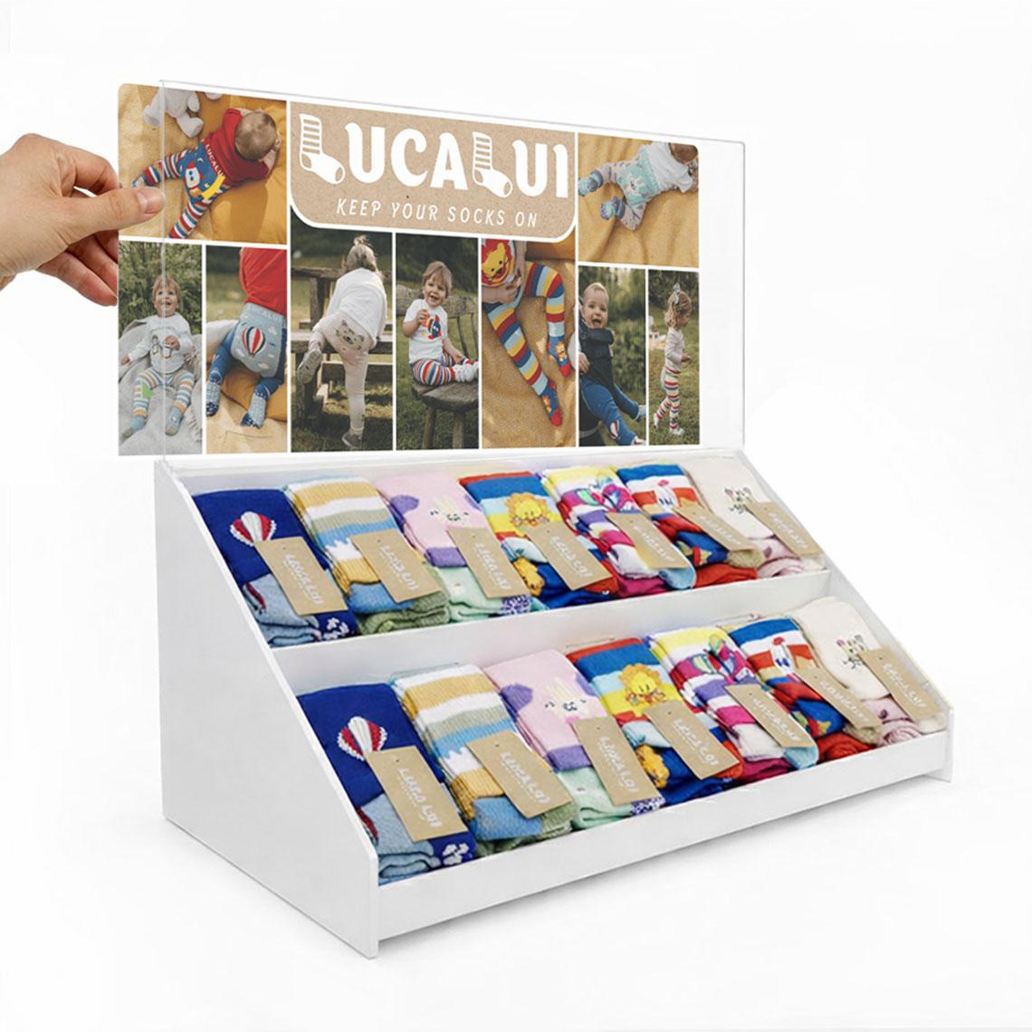Countertop point of purchase display featuring interchangeable side-loading graphic trap header with promotional insert above two tiers of retail shelving.