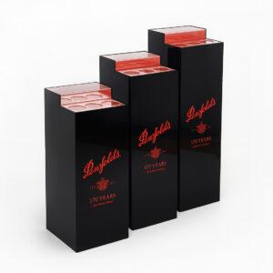 Three glossy black Penfolds display plinths of varying heights stand on a seamless white floor and background. Each plinth has a red-tinted top section with circular cutouts for holding bottles, and features bold red Penfolds branding and “170 Years of Winemaking” printed on the front.
