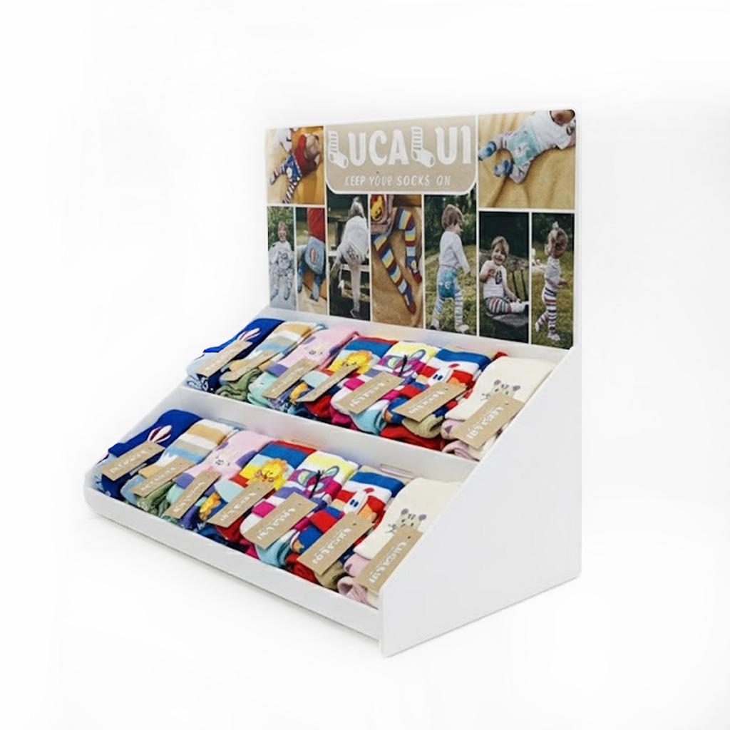 White left-facing countertop point-of-purchase display showcasing folded patterned socks, with an integrated branded header panel displaying lifestyle photos.