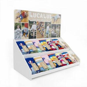 White right-facing countertop point-of-purchase display holding neatly folded colorful socks, featuring a branded backboard with lifestyle imagery.
