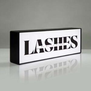 An illuminated lightbox with a black outer frame and "lashes" printed onto it.