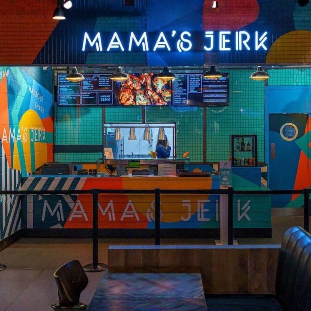 A Mama's Jerk restaurant counter with digital screens hanging above the till.