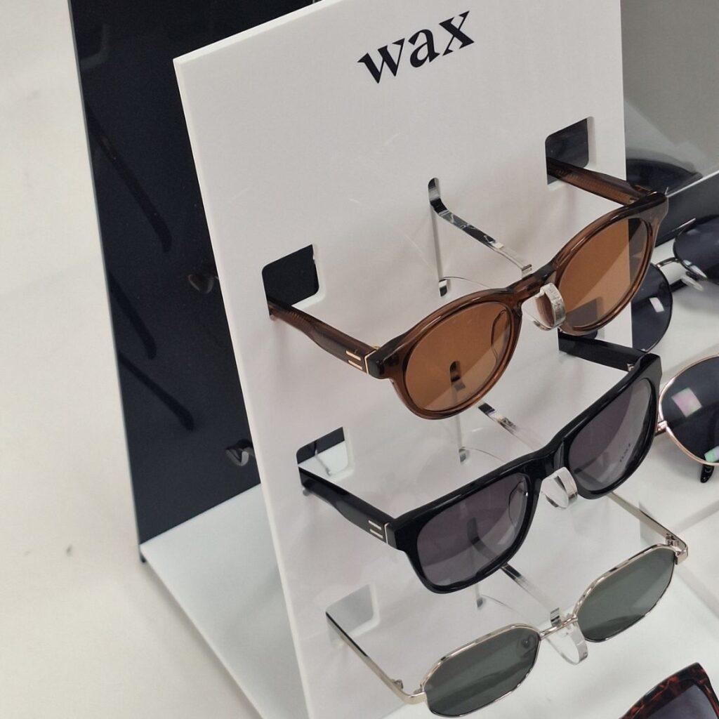 Side detail of the custom WAX sunglasses display stand highlighting the three-hook merchandising system, digitally printed branding, and black and white acrylic construction.