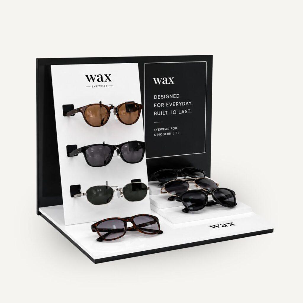 Angled view of the custom WAX sunglasses display stand showcasing multiple eyewear styles, digitally printed branding, and a layered acrylic merchandising design.