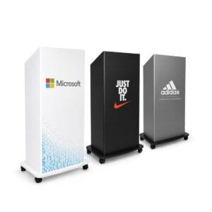 Three branded portable presentation lecterns in white, black and grey finishes displayed in a clean studio setting, featuring custom corporate branding designs on mobile podium stands with lockable castor wheels.